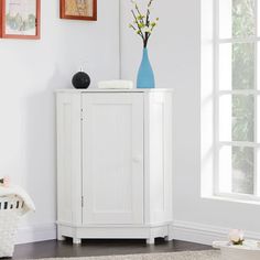 a white cabinet sitting in the corner of a room with pictures on the wall behind it