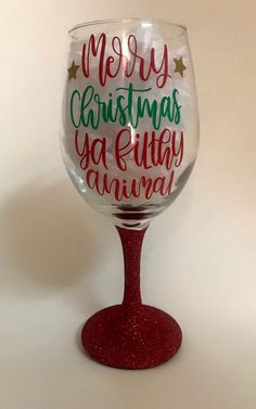 a wine glass that says merry christmas ya filthy animal on the bottom, and red base