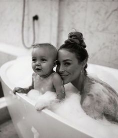 a woman holding a baby in a bathtub filled with foamy water and bubbles