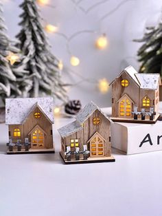 three small wooden houses sitting on top of a white box with christmas lights in the windows