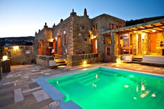 an outdoor swimming pool at night with lights on the house and patio area in the background