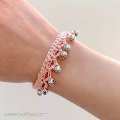 a woman's arm wearing a pink crochet bracelet with silver balls on it