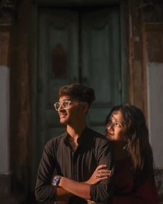 two people standing next to each other in front of a door with the light shining on them