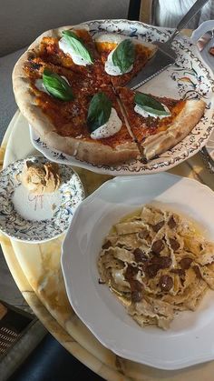 a pizza sitting on top of a white plate next to pasta and sauces in bowls