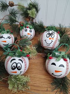 four baseball ornaments with faces painted on them sitting on a table next to pine branches