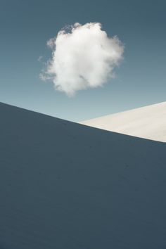 a lone cloud is in the sky above a snow - covered hill with no one on it