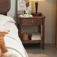 a nightstand with a lamp on it next to a bed