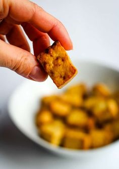 a hand holding a piece of bread over a bowl full of small cubed food