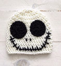 a crocheted skull hat with black eyes on white wood background, top view