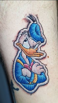 a tattoo with a cartoon duck holding a baby in it's arms and wearing a blue hat