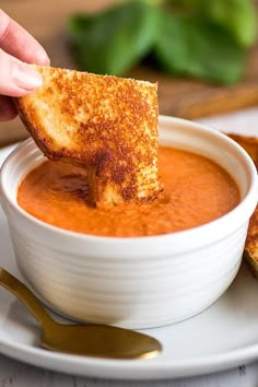 a person dipping some bread into a bowl of tomato soup