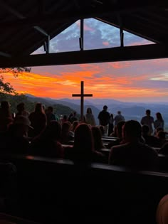 a group of people sitting in front of a cross on top of a hill at sunset