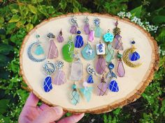 a person holding up a wooden slice with many different colored earrings hanging from it's sides