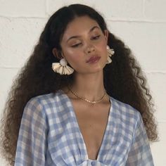 a woman with long curly hair wearing a blue and white checkered shirt, gold chain necklace and matching earrings