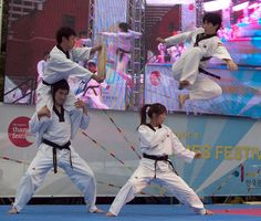 three people doing karate moves in front of a large screen with an advertisement on it