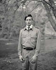 a black and white photo of a man in uniform standing under a tree with his hands on his hips