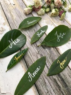 some leaves with names on them sitting on a wooden table next to flowers and greenery