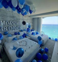 blue and white balloons are hanging from the ceiling above a bed in a room with an ocean view