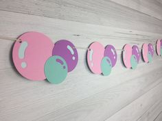 a number of pink and green circles hanging from a line on a wall with wooden planks