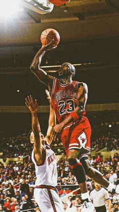 two men playing basketball in front of an audience at a sporting event, one jumping for the ball