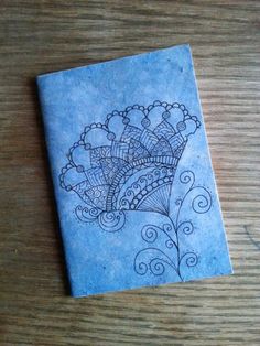 a drawing on a piece of blue paper sitting on top of a wooden table next to a cell phone