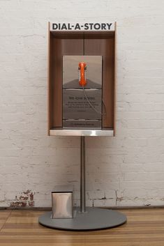 a display case with an orange object in it on top of a wooden floor next to a white brick wall