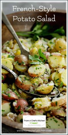 a bowl filled with potatoes and herbs on top of a wooden table next to a spoon