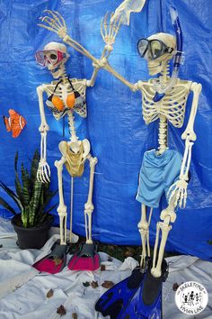 two skeletons in scuba gear standing next to each other on a blue sheet covered ground