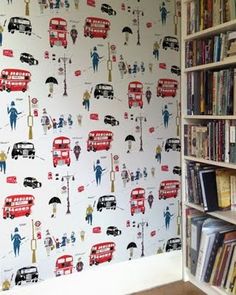 a book shelf filled with books next to a wallpaper covered in red double decker buses