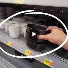 a person holding a black bowl on top of a shelf next to white mugs