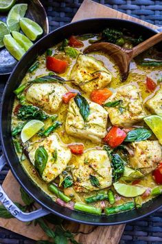 a pan filled with tofu and vegetables on top of a wooden cutting board next to limes