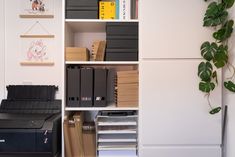 a white book shelf filled with books next to a printer and other office supplies on top of it