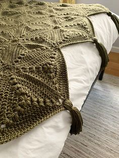 a crocheted blanket with tassels on top of it sitting on a bed