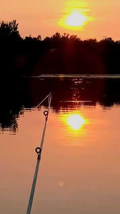 the sun is setting over water with a fishing pole in it's foreground