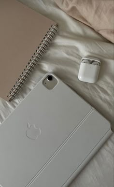 an apple laptop computer sitting on top of a bed next to a notebook and headphones