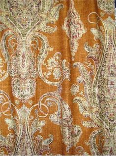 an orange and white paisley print curtain with fringes on the bottom, in front of a