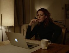 a woman sitting at a table in front of a laptop computer with a cup of coffee next to her