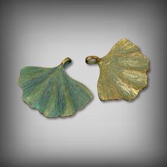 two green and gold leaf shaped pendants on a gray background, one is open