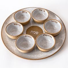 six gold and white bowls on a plate with the word god written in hebrew above them