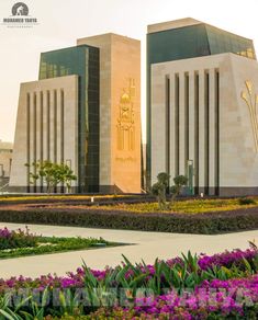 the building is very large and has many flowers in front of it, including purple flowers