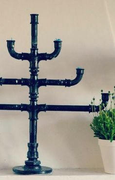 a candle holder made out of pipes is sitting on a shelf next to a potted plant