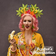 a woman with pink hair is holding a banana and wearing a headdress that has horns on it