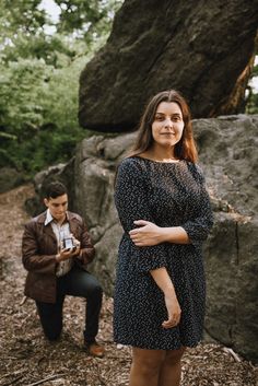 a woman standing next to a man in front of a large rock with trees behind her