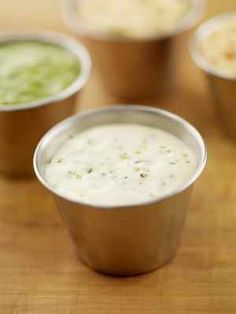 four cups filled with different types of dips on a wooden table in front of them