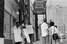 black and white photograph of people holding signs in front of a building on the street