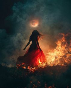 a woman standing in front of a fire with the moon above her head and arms outstretched