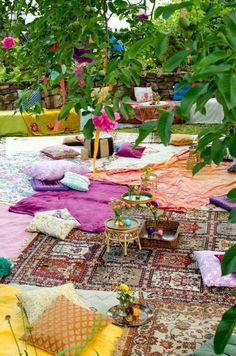 an outdoor area with lots of colorful rugs and pillows on the ground in front of trees