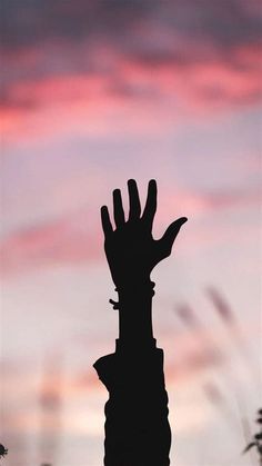 a silhouette of a hand reaching up into the sky at sunset or dawn with pink clouds in the background