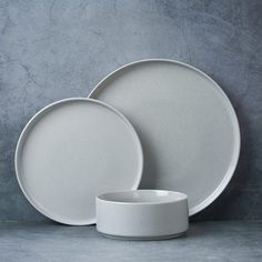 three white plates and one bowl on a grey surface with a gray wall in the background