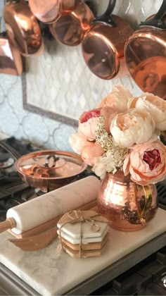 a vase filled with flowers sitting on top of a counter next to copper pans